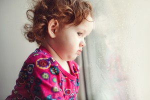 Sad little girl looking out the window.